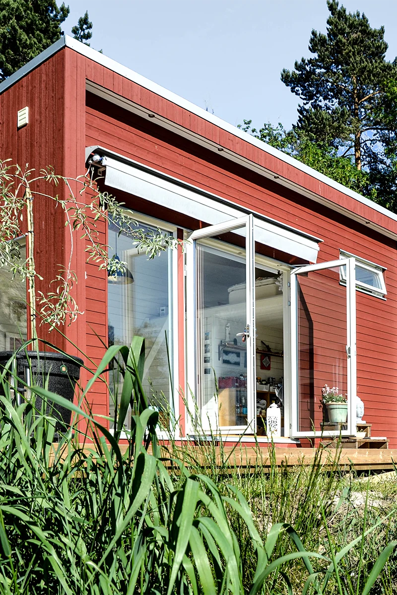 Rött attefallshus med atelje, två öppna fönsterdörrar, i en trädgård