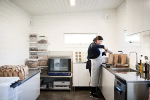 Attefallshus som arbetsplats med industrikök. Kvinna häller upp musli i förpackningar på bänken