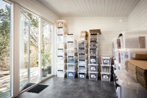 Förvaring står staplad längs en vägg i vit träpanel, till vänster två fönsterdörrar ut till altan