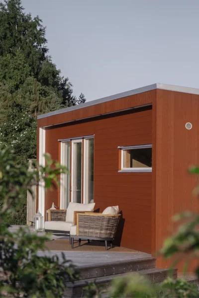 Rött bastuhus med altan framför. Huset har fyra fönster