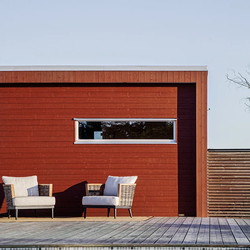 Rött bastuhus med altan och pool framför. Huset har ett avlångt liggande fönster