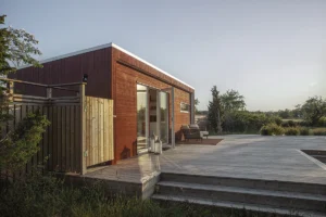 Rött bastuhus med öppen fönsterdörr och en stor altan framför