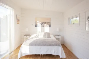 Sovplats med dubbelsäng i ett bastuhus. Vit träpanel med tavlor på