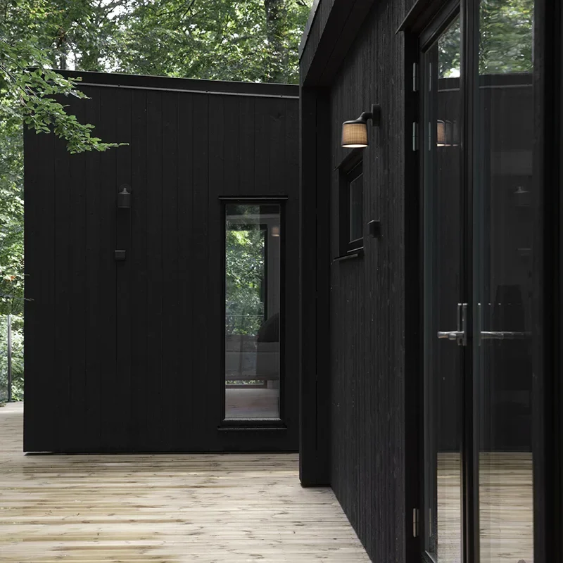 Enkelrum Nest med två hus i vinkel med svart träpanel, stora fönster och träaltan