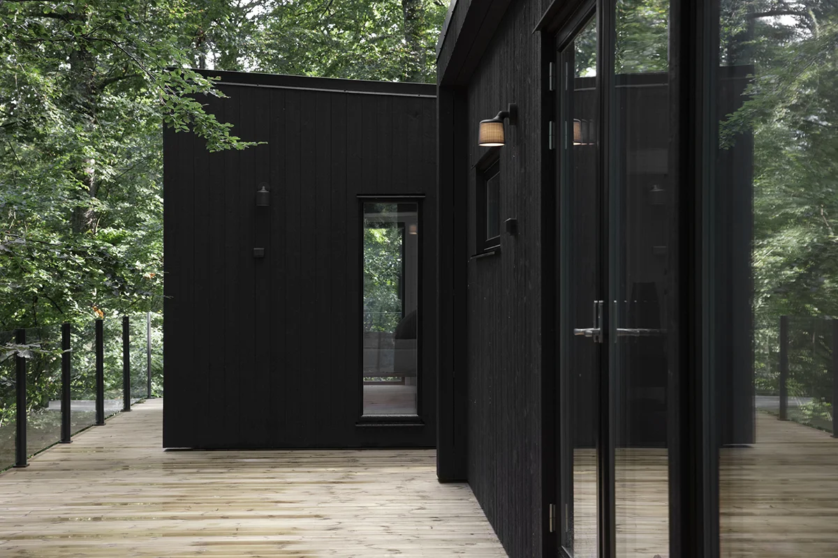 Exteriör i svart träpanel, stora fönster, fönsterdörrar och träaltan på Enkelrum Nest