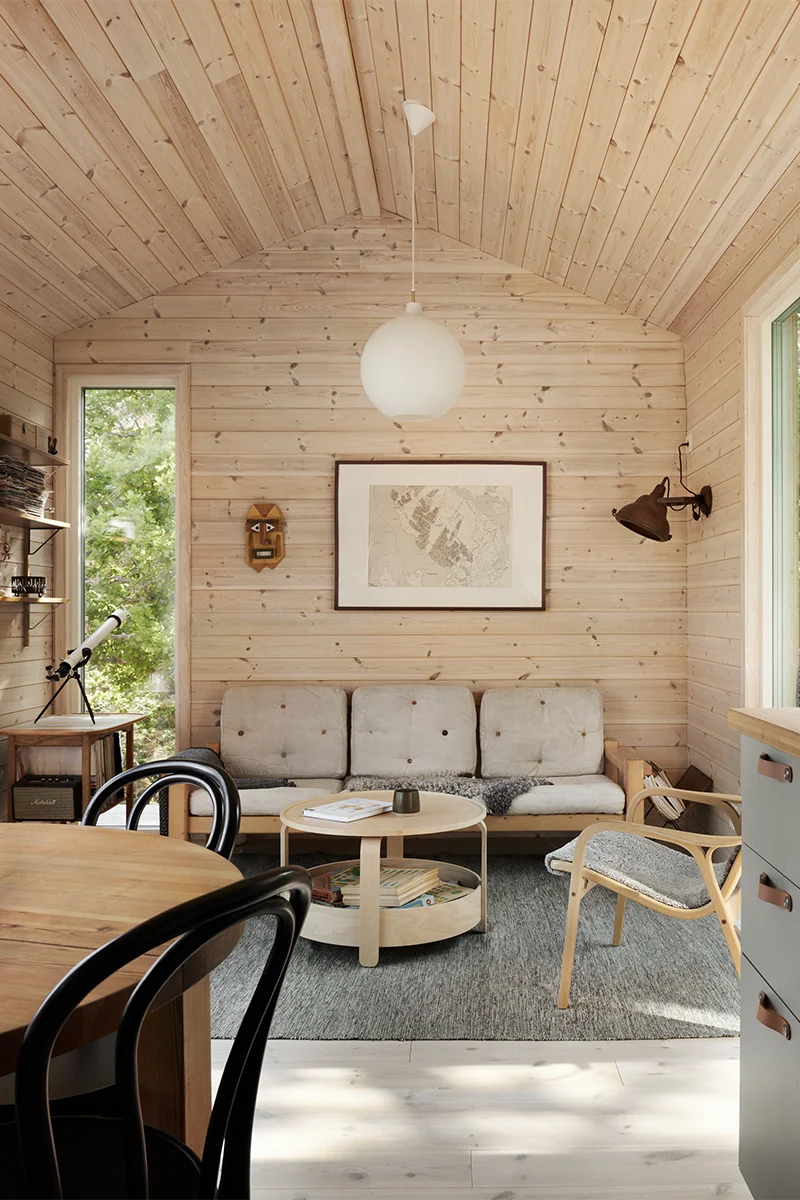 Rum med träpanel i visningshuset på Djurö, inrett med soffhörna och sidobord med kikare på