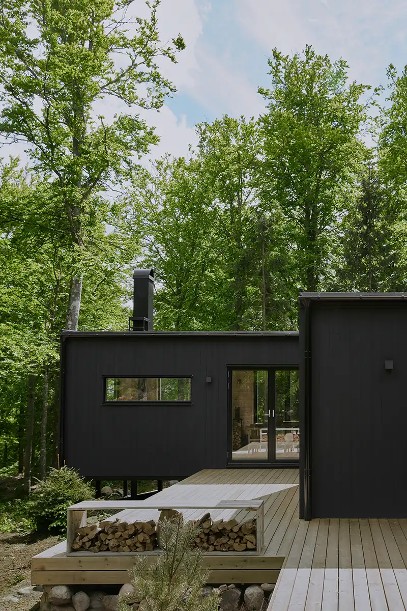 Svart modulhus 90 kvm med stora fönster och träaltan i en grön skog