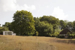 Miljöbild visar en skog med attefallshus till vänster och gammalt hus till höger