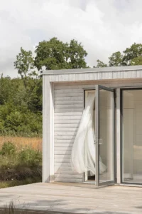 Gardin blåser genom en öppen dörr i ett attefallshus i trä