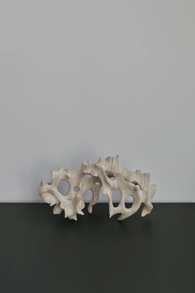 Träskulptur på en grön skiva mot vit vägg