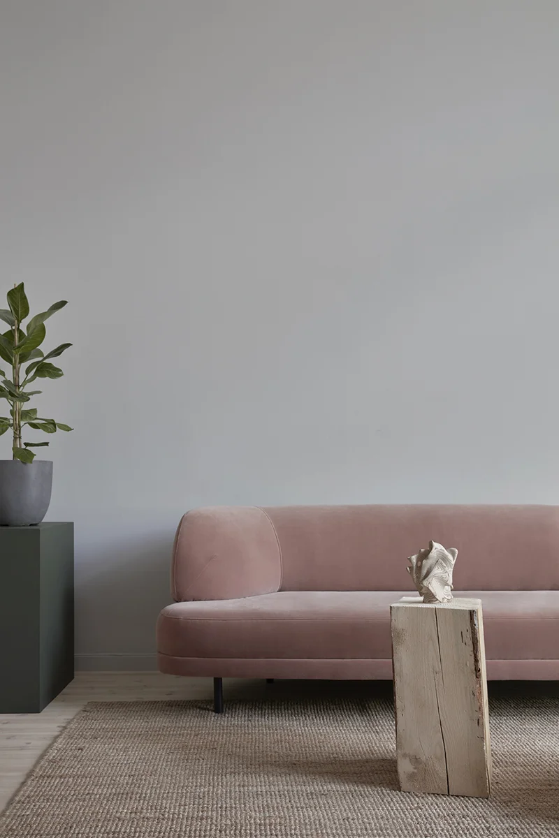 Rosa soffa med träpiedestal framför står på en beige matta. Växt i hörnet på grön piedestal