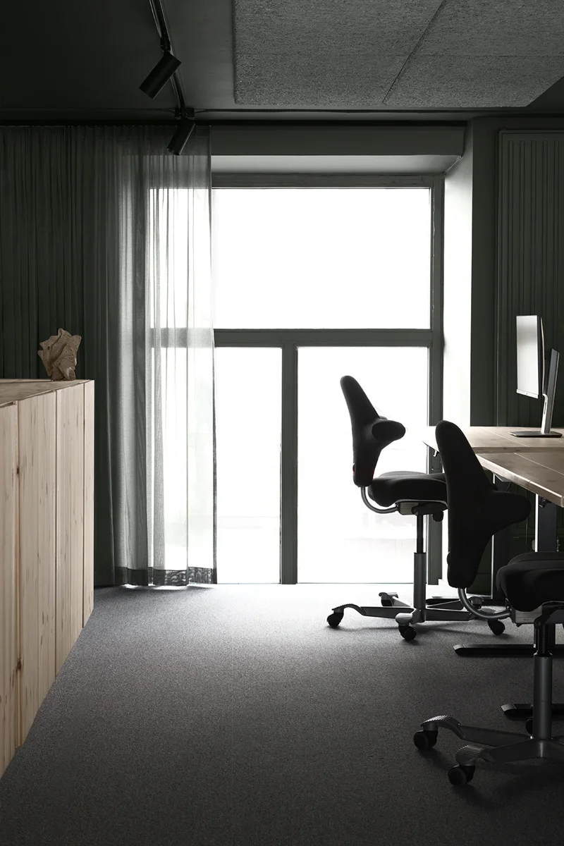 Kontorsplatser med skåp bakom, vid ett stort fönster med grön gardin