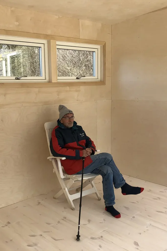 Man sitter i en plaststol inne i huset med plywoodväggar