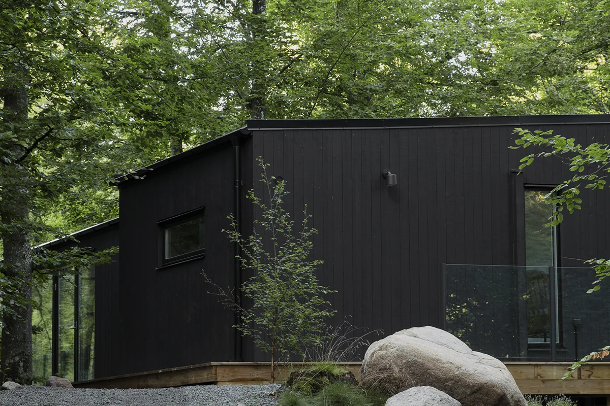 Utsiden av Enkelrum Nest i svartmalt trepanel i en grønn skog