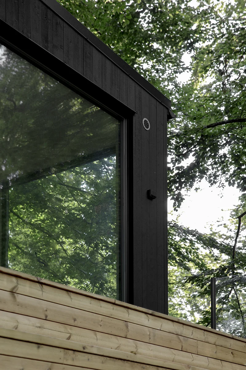 Detalj av Enkelrum Nests svarte trepanel og store vinduer, omgitt av grønne trær