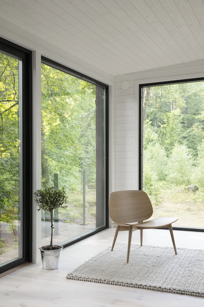 Stue i enkeltrom med lenestol ved siden av en potteplante i et hjørne med vinduer på begge veggene