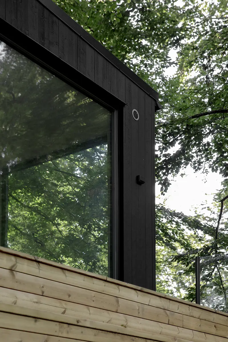 Detail of Nest's black wooden panel, large windows, surrounded by green leaves